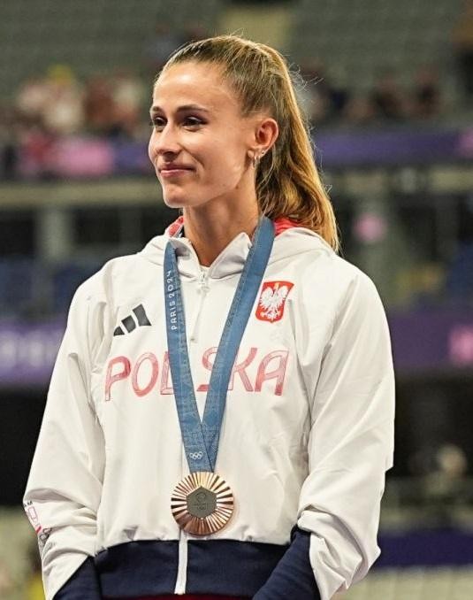 Natalia Bukowiecka na bieżni, uśmiechnięta, w pozycji biegowej, na tle słonecznego stadionu.