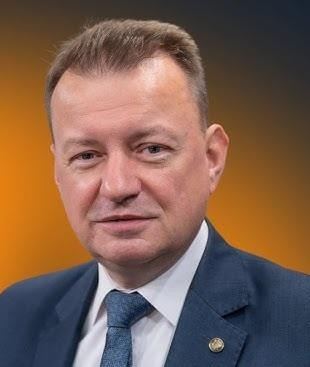 Alt: Mariusz Błaszczak jako Minister Obrony Narodowej, w otoczeniu żołnierzy lub sprzętu wojskowego, podczas inspekcji lub ćwiczeń.