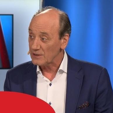 Dariusz Szpakowski, polski komentator sportowy, z ekspresywną miną podczas komentowania meczu, w tle rozmyty stadion piłkarski.