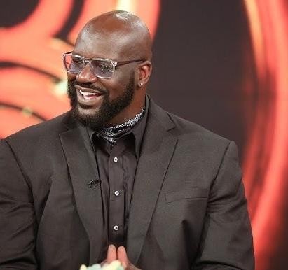 Shaquille O'Neal uśmiechnięty i charyzmatyczny, z elementami koszykówki i studia w tle, symbolizującymi jego wszechstronną karierę.