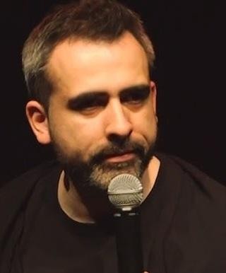 Abelard Giza na scenie podczas występu stand-upowego, z mikrofonem w dłoni, dynamicznie gestykulujący, prezentujący swoją charyzmę i inteligentny humor.