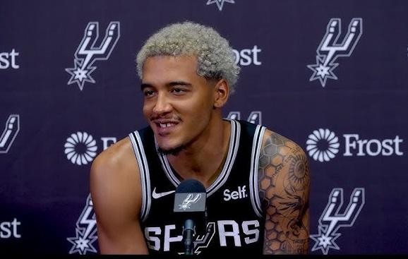 Jeremy Sochan dumnie pozujący w koszulce San Antonio Spurs na boisku do koszykówki.