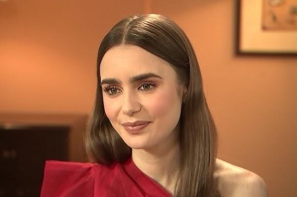 Lily Collins uśmiechnięta, przeglądająca Instagram na telefonie, w nowoczesnym wnętrzu, symbolizująca jej aktywność w mediach społecznościowych.